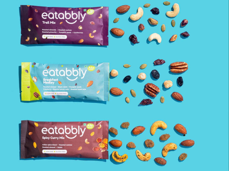 Multiple packets of Eatabbly fruit and nut mix on a blue background
