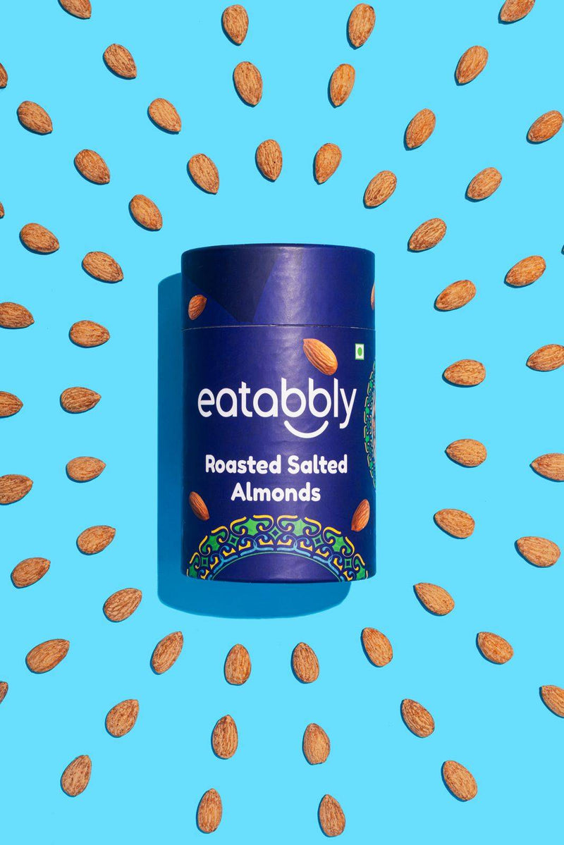 Blue container of eatabbly roasted salted almonds on a blue background with scattered almonds.